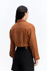 Campera corta tipo gamuza con textura suave y acabado mate. Presenta cuello camisero, cierre frontal con botones oscuros y dos bolsillos frontales de parche. Su diseño es de silueta cropped.