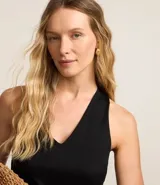 Vestido midi de corte evasé confeccionado en tejido piquet color negro. Presenta un diseño sin mangas con escote en V, breteles anchos cruzados en la espalda con detalle de nudo y falda con recortes de volados en la parte inferior.