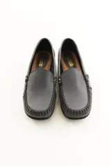Mocasín de cuero vacuno color negro, con costuras artesanales visibles alrededor de la puntera y suela de perfil bajo.
