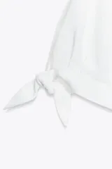 Camisa de manga corta confeccionada en tejido de ramio color blanco. Posee cuello solapa, cierre frontal con botones y detalle de lazos en el acabado de las mangas.