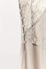 Vestido largo de viscosa con escote en pico, aplicación de encaje a tono en el busto, tirantes finos y diseño drapeado. Cuenta con forro interior y cierre lateral con botones forrados.