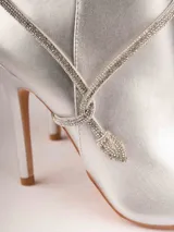 Botines plateados con terminación en punta y taco aguja. Decorados con tiras de strass que se enrollan alrededor del tobillo y se atan en el empeine.