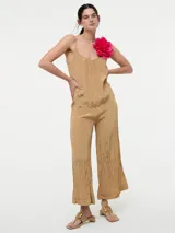 Mono largo color beige con textura arrugada, breteles finos regulables y detalle de flor fucsia en el hombro.