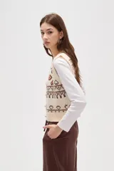 Chaleco tejido de punto con diseño jacquard de corazones y motivos geométricos en tonos verde y rosa. Presenta escote en V, cierre frontal con botones y terminaciones acanaladas en cuello, sisas y ruedo.