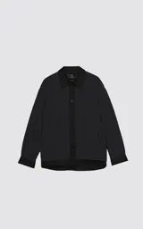 Campera tipo sobrecamisa de diseño oversize, confeccionada en microfibra opaca con patrón matelaseado geométrico. Presenta cuello, puños, cartera central y ruedo en gabardina de algodón, con cierre frontal mediante broches a presión. El diseño del ruedo simula una prenda superpuesta.