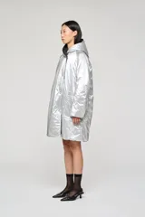 Campera reversible de corte regular, confeccionada en nylon con acabado repelente al agua. Presenta diseño con capucha, mangas raglán y cierre frontal con botones. Un lado es de color negro con bolsillos de parche, mientras que el reverso es de color plateado con bolsillos laterales integrados.