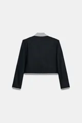 Blazer corta de color negro con cuello solapa, manga larga y hombreras. Presenta detalles combinados con estampado de cuadro vichy en el cuello, los bordes de la solapa, el ruedo y los puños. Cuenta con cierre frontal de un botón y falsos bolsillos delanteros de vivo.