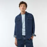 Camisa de denim azul con diseño de rayas verticales finas y blancas, manga larga con puños ajustables, cierre frontal de botones y dos bolsillos de parche con solapa en el pecho.