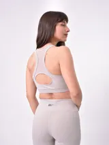 Top deportivo de color taupe con diseño de cuello redondo y panel central de malla transparente. Presenta un corte ajustado con banda elástica inferior para mayor soporte.