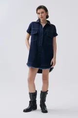 Vestido corto de denim azul oscuro, con cuello camisero, mangas cortas con dobladillo y cierre frontal con botones. Tiene bolsillos en el pecho y laterales, y cinturón de pañuelo estampado.