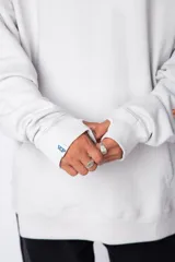 Buzo canguro oversize de algodón rústico, color gris claro, con capucha y cordones ajustables con logo estampado. Presenta un diseño gráfico pequeño en el pecho y detalles estampados en la manga.