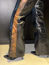 Pantalón de cuero negro con paneles laterales de cuero invecchiato con efecto desgastado. Presenta un diseño de cordones laterales a lo largo de las piernas y ajuste en la cadera, con corte recto y ligeramente acampanado.