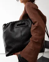 Bolso tipo tote color negro, confeccionado en cuero, con diseño de frunces en la parte superior y abertura integrada para llevar en la mano o al hombro.
