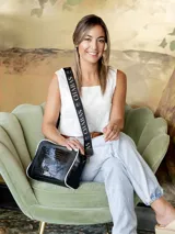 Bandolera negra de cuero con textura de cocodrilo, correa ancha con el nombre de la marca y detalles en blanco.