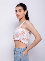 Top blanco con estampado floral en tonos naranja y lila, de corte cropped y breteles anchos.