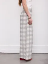 Pantalón de corte ancho y fluido, con estampado a cuadros en tonos grises y blancos, cintura alta con trabillas y bolsillos laterales.