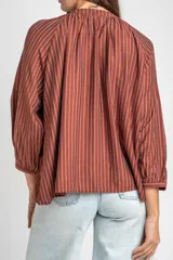 Blusa de manga larga con diseño a rayas verticales, cuello redondo con pequeña abertura frontal abotonada y mangas con puños elásticos.