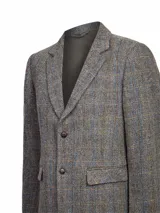 Blazer de lana Harris Tweed con patrón de espiga y cuadros sutiles en tonos tierra, azul y naranja. Presenta cierre frontal de dos botones, solapas clásicas y bolsillos con solapa. Incluye forro interior satinado.