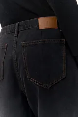 Pantalón de denim fino color negro con un dejo de marrón, tiro medio y pata ancha con costuras a contratono.