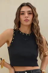 Musculosa crop de morley negro con cuello redondo, decorada con tachas en forma de estrella doradas a lo largo del cuello y sisas. Cuenta con un pequeño bordado frontal en el centro del pecho.