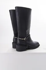 Bota de cuero negra con caña media, taco cuadrado y detalle de correa con pieza metálica plateada alrededor del tobillo.