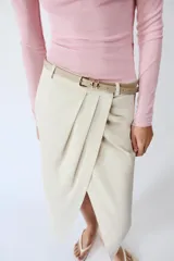 Falda midi de tiro medio color beige, con pliegues en la parte delantera, abertura frontal en el bajo y cinturón combinado a tono con hebilla metálica.