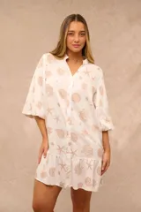 Vestido corto blanco con estampado marino de caracoles y estrellas de mar en tonos tostados, escote en V con cuello mao, mangas 3/4 y volado en el ruedo.