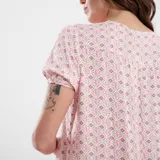 Vestido midi de corte recto, con estampado floral en tonos rosa y naranja sobre fondo crudo. Presenta cuello en V, mangas cortas y ruedo con volantes.
