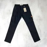 Pantalón cargo de gabardina color negro, con bolsillos laterales con solapa y cierre de botón. Presenta un parche de cuero sintético en uno de los bolsillos laterales.