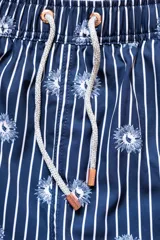 Short de baño azul marino con rayas verticales blancas y estampado de flores azules. Cuenta con cintura elástica con cordón regulable, bolsillos laterales y bolsillo trasero con cierre.