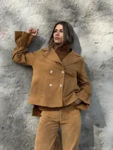 Chaqueta color tostado de corte recto y diseño cruzado con doble botonadura frontal. Presenta cuello solapa y mangas largas con puños acampanados y fruncidos.