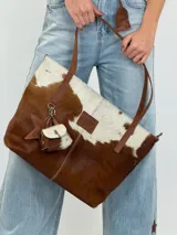 Bolso tipo tote Chabas modelo Molly, confeccionado en cuero con pelo natural en tonos marrón y blanco. Posee asas largas de cuero marrón, parche frontal con la marca grabada y un charm colgante decorativo en forma de estrella con detalle de pelo.