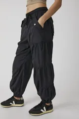 Pantalón jogger negro de inspiración utility, confeccionado en tejido liviano de poliamida. Cuenta con cintura elástica ajustable con cordón, bolsillos cargo con broches metálicos, diseño con paneles fruncidos y puños elastizados.