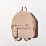 Mochila pequeña de nylon color beige con cierre superior y bolsillo frontal con cierre. Tiene asa de mano y correas ajustables para los hombros.