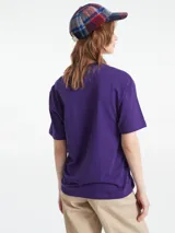 Remera de manga corta color morado oscuro, corte holgado, con estampado frontal en blanco con la marca "Carhartt" en tipografía gótica y el texto "Work in Progress" debajo.