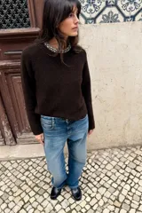 Jersey de punto color marrón oscuro, de corte recto y manga larga. Presenta un cuello redondo decorado con abalorios joya y una abertura en la espalda con cierre de botón.