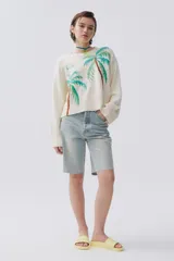 Sweater tejido de punto color crudo, con bordados de palmeras y la frase 'Bikini Beach' en el frente. Tiene detalles calados en las sisas y mangas.