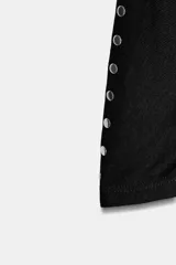 Camiseta de cuello barco y manga larga tipo murciélago, confeccionada en tejido de punto gris melange. Presenta detalle de tachas metálicas a lo largo de los hombros y las mangas.