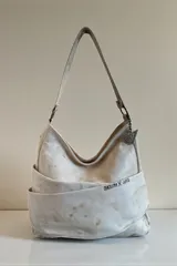 Cartera tipo hobo de cuero natural con efecto desgastado, diseño envolvente, manija de hombro y detalle de la marca escrito en el frente.