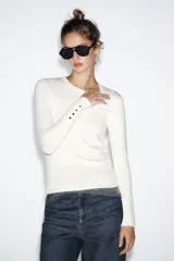 Jersey Zara de punto liso color negro, con cuello redondo, manga larga y detalle de botones dorados en los puños.