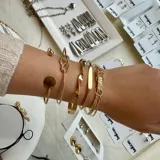 Set de cinco pulseras doradas de diferentes diseños: una con un círculo, otra con un nudo, otra lisa, otra con un diseño trenzado y otra con un nudo.