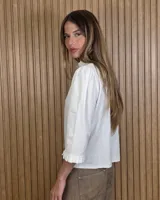 Camisa de algodón color blanco con rayas verticales rosadas, cuello alto con volados, mangas tres cuartos abullonadas con puños elastizados con volados y cierre frontal de botones oscuros.