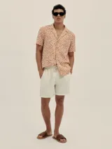 Camisa de manga corta con cuello estilo cubano y estampado de manchas color naranja sobre fondo blanco.