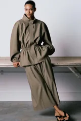 Pantalón culotte de tiro medio, con diseño de pierna ancha y pliegues frontales. Cuenta con cintura ajustable mediante cordones, bolsillos laterales y cierre frontal con cremallera y gancho metálico.