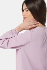 Blusa de manga larga con cuello redondo y cierre frontal parcial mediante botones forrados. Presenta diseño de doble capa en el frente y puños abotonados.