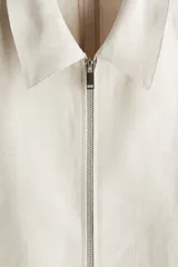Campera color crema confeccionada en mezcla de lino y viscosa, con cuello clásico, cierre frontal, bolsillos laterales insertados al bies con botón a presión oculto, costura decorativa en la espalda y botón a presión en los puños.