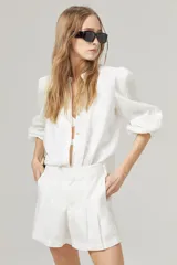 Short de lino blanco con cintura alta, tablas, bolsillos laterales y cierre frontal con gancho metálico.