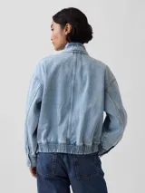 Campera bomber de jean con lavado claro, cuello alto con botones a presión, cierre frontal, bolsillos con solapa en el pecho y elástico en el dobladillo inferior y los puños.