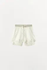 Bermuda de algodón blanca de tiro medio, con cintura elástica ajustable mediante cordón. Cuenta con delicados bordados florales y detalles de encaje a tono, con bajo acabado en ondas y aberturas laterales.