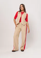 Chaleco beige con escote en V, sin mangas y cierre frontal con botones. Presenta pespuntes en color rojo y logo bordado en la espalda.